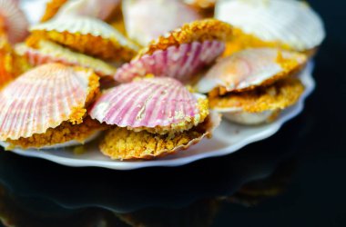 Üzerinde kabuk olan bir tabak yemek. Kabuklar pembe ve beyaz. Plakası siyah arka planda.