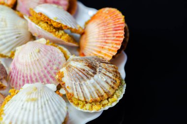 Üzerinde kabuk olan bir tabak yemek. Kabuklar pembe ve beyaz. Plakası siyah arka planda.