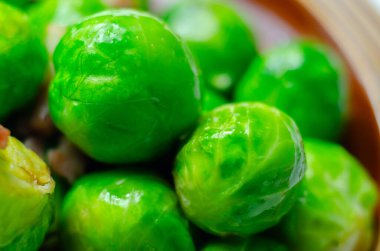 Üstünde pastırma olan bir tabak yeşil Brüksel lahanası. Pastırma filizlerin üzerine yayılmış, onlara lezzetli ve çıtır çıtır bir doku veriyor.