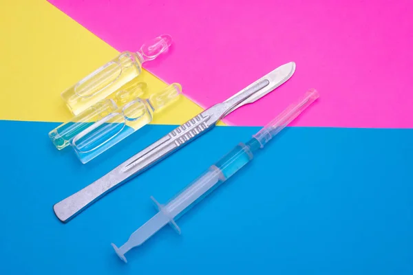 Ampoules, scalpel, syringe (medical materials for treatment) lie on a background of yellow, pink, blue. A photograph for use in a medical advertisement or presentation.