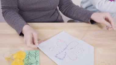 Küçük kız annesiyle el sanatları masasında dikiş dikmeyi öğreniyor..