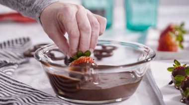 Adım adım. Çikolata kaplı çilek hazırlamak için organik çilekleri erimiş çikolatayla bir kaseye daldırmak..