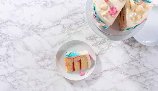 Flat lay. Slice of a mermaid-themed 3 layer vanilla cake with chocolate mermaid tails and seashells on a white plate.