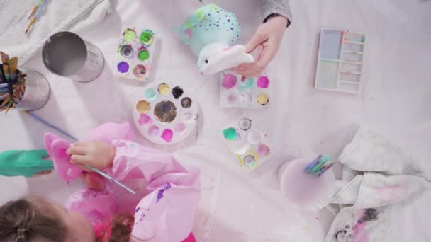 平躺在床上小女孩为她的家庭教育艺术项目用丙烯酸涂料画纸巾和雕像 — 图库视频影像