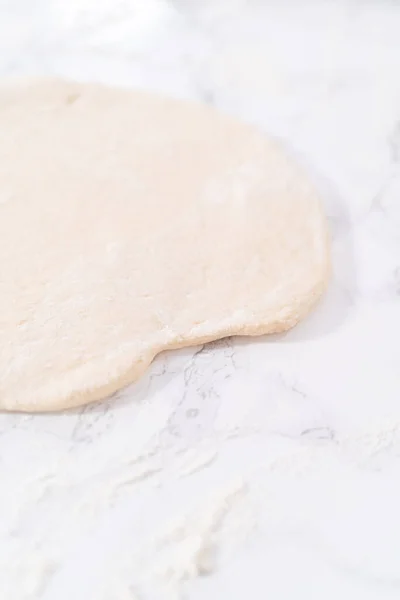 Rolling pizza dough with a french rolling pin to prepare cinnamon dessert pizza.