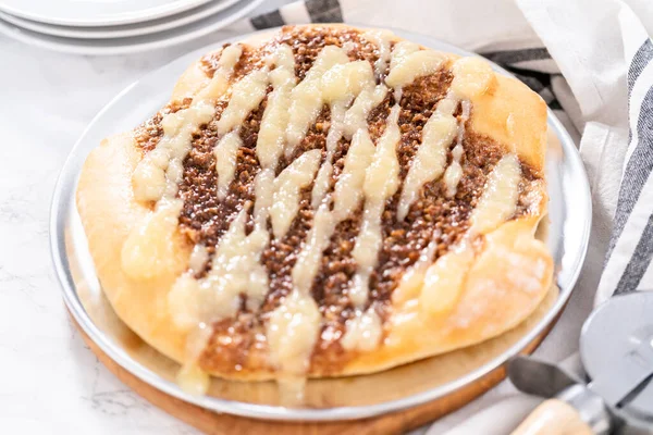 Freshly baked cinnamon dessert pizza with cream cheese drizzle.