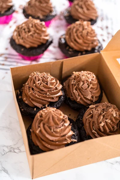 Packaging chocolate cupcakes with chocolate ganache frosting into a paper cupcake box.