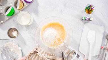 Düz yatıyordu. Adım adım. Vanilyalı Mardi Gras kekleri pişirmek için karışımı elektrikli mikserle karıştırıyorum..