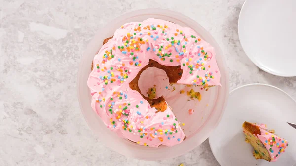 平置きだ 一歩ずつ 上にピンクのバタークリームのフリストと内側にバタークリームの充填でFunfettiバントケーキをスライス — ストック写真