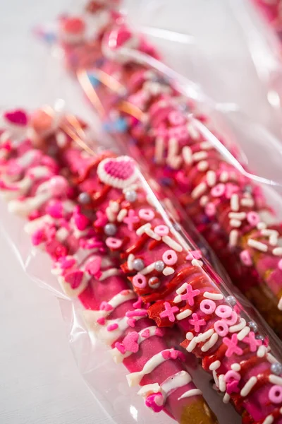 チョコレートで覆われたプレッツェルロッドは 明確な袋に詰められたバレンタインデーのためのハート型のスプリンクルで飾られています — ストック写真