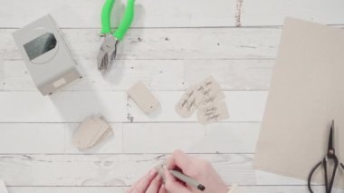 Düz yatıyordu. Adım adım. Kahverengi kağıttan hediye etiketlerini kağıt punçla kesiyor..