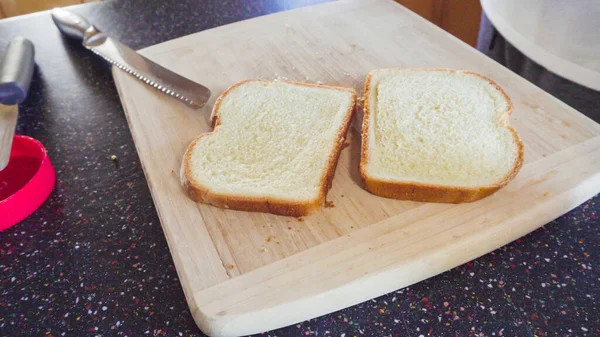 Preparing peanut butter and jelly sandwich on a wood cutting board.