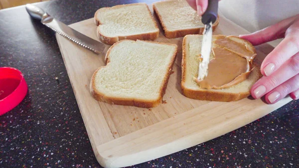 Preparing peanut butter and jelly sandwich on a wood cutting board.