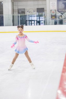 Küçük kız buz pateni pistinde artistik patinaj yapıyor..