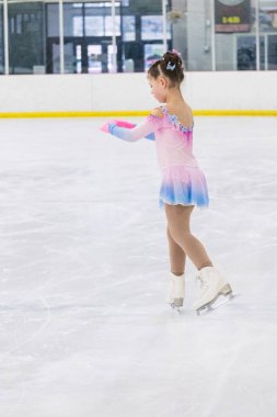 Küçük kız buz pateni pistinde artistik patinaj yapıyor..