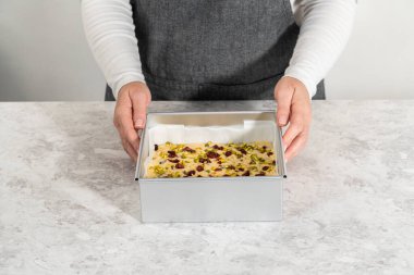 Parşömenle kaplı kare bir cheesecake tavasından kızılcık fıstıklı şekerlemeyi kaldırmak.