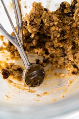 Yumuşak yulaf ezmeli, cevizli, kuru üzümlü kurabiye pişirmek için parşömen kağıdıyla kaplı bir yemek tepsisine hamur kepçesiyle kurabiye pişirmek..