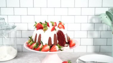 Step by step. Slicing red velvet bundt cake with cream cheese frosting garnished with fresh strawberries.
