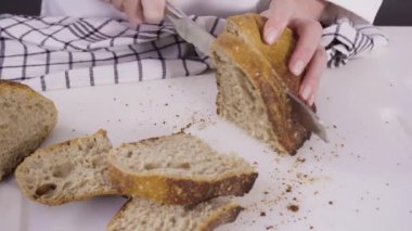 Beyaz bir kesme tahtasının üzerinde taze ekşi ekmek dilimliyorum..