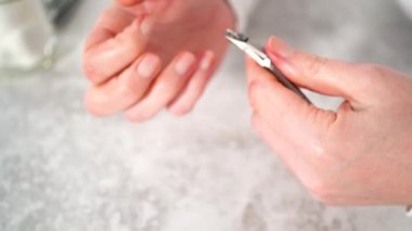 Kadın manikürünü evde basit manikür aletleriyle bitiriyor. Tırnakların etrafındaki tırnak etlerini kesiyor..