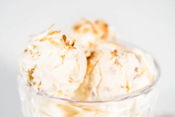 Homemade coconut ice cream garnished with roasted coconut flakes in a glass ice cream bowl.