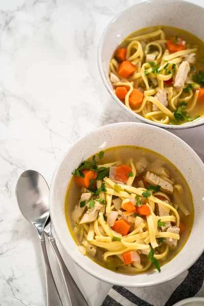 Serving chicken noodle soup with kluski noodles in white ceramic soup bowls.
