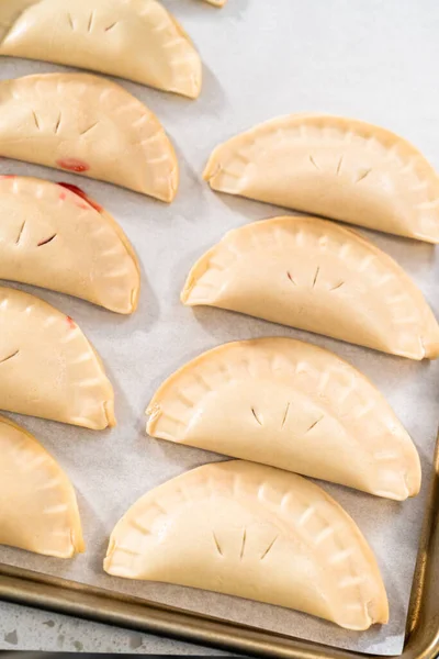 Unbaked sweet cherry empanadas on a baking sheet lined with a parchment paper baking sheet.