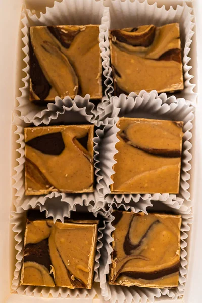 Packaging homemade chocolate fudge with peanut butter swirl into a white gift box.