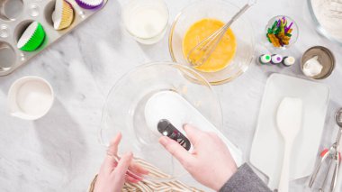 Düz yatıyordu. Adım adım. Vanilyalı Mardi Gras kekleri pişirmek için karışımı elektrikli mikserle karıştırıyorum..