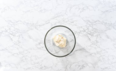 Flat lay. Whisking buttercream frosting in a glass mixing bowl with an electric hand mixer to prepare the peppermint buttercream frosting.