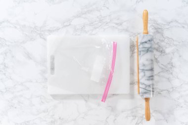 Flat lay. Crushing peppermint candies in a plastic bag with a marble rolling pin on a white cutting board.