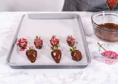 Çikolata kaplı çilekleri hazırlamak için erimiş çikolataya çilek bandırıyorum..