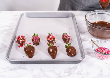 Çikolata kaplı çilekleri hazırlamak için erimiş çikolataya çilek bandırıyorum..