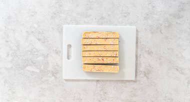 Düz yatıyordu. Büyük bir mutfak bıçağıyla şeker kamışı şekerlemesini beyaz bir kesme tahtasında kare parçalara ayırmak..