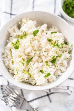 Cilantro Lime Rice. Beyaz seramik kaselerde taze maydanozla süslenmiş kişniş limonlu pirinç servis ediliyor..
