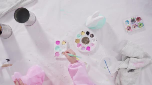 平躺在床上小女孩为她的家庭教育艺术项目用丙烯酸涂料画纸巾和雕像 — 图库视频影像