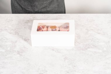 Taze pişmiş çikolatalı, gurme pembe çikolatalarla süslenmiş kapkek paketleri beyaz kağıt kek kutusuna konuyor..