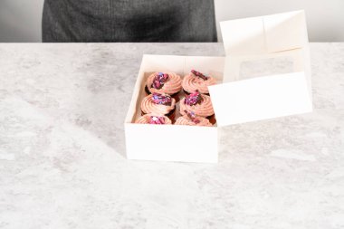 Taze pişmiş çikolatalı, gurme pembe çikolatalarla süslenmiş kapkek paketleri beyaz kağıt kek kutusuna konuyor..