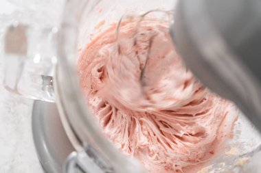 Whipping strawberry buttercream frosting in a stand-alone electric mixer with a whisk attachment. clipart