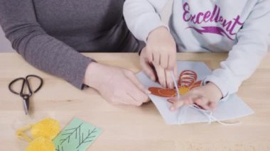 Küçük kız annesiyle el sanatları masasında dikiş dikmeyi öğreniyor..