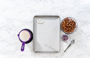 Flat lay. Dipping pretzels twists into melted chocolate to make red, white, and blue chocolate-covered pretzel twists.