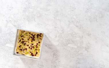 Düz yatıyordu. Kızılcık fıstıklı şekerleme hazırlamak için parşömen kağıdıyla kaplı kare cheesecake tavası..