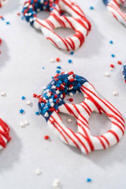 Dipping pretzels twists into melted chocolate to make red, white, and blue chocolate-covered pretzel twists.