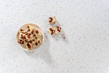 Düz yatıyordu. Beyaz seramik tabakta ev yapımı beyaz çikolatalı fındıklı şekerleme parçaları..