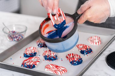 Dipping pretzels twists into melted chocolate to make red, white, and blue chocolate-covered pretzel twists.