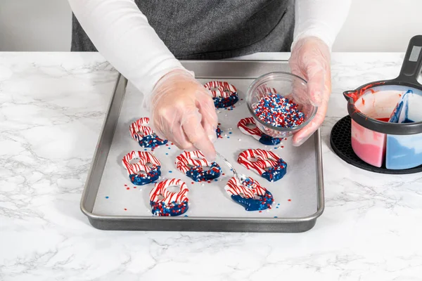 Flat lay. Dipping pretzels twists into melted chocolate to make red, white, and blue chocolate-covered pretzel twists.