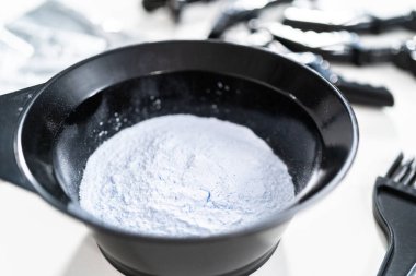 Siyah plastik bir kasede beyaz arka planda saç boyası tozu..