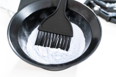 Siyah plastik bir kasede beyaz arka planda saç boyası tozu..