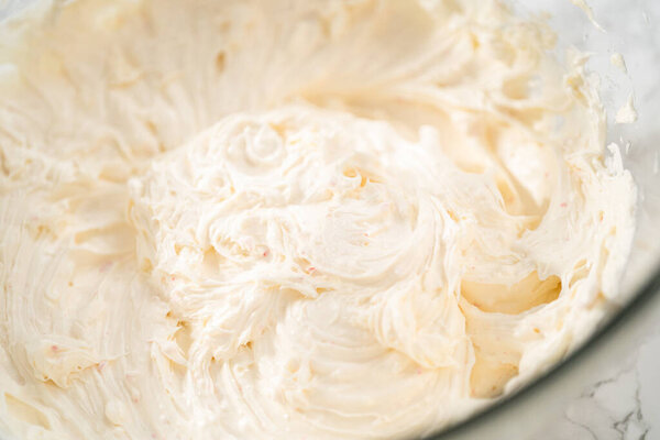 Whisking buttercream frosting in a glass mixing bowl with an electric hand mixer to prepare the peppermint buttercream frosting.