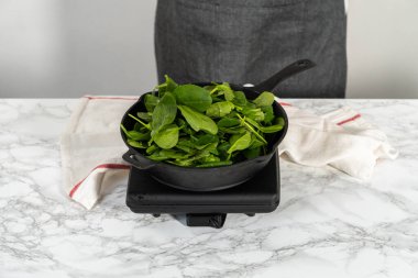 Adım adım. Ispanak ve jambonlu frittata hazırlamak için sobanın üzerinde dökme demir tava var..